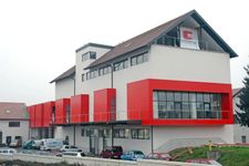 Večnadstropna bela stavba fizične vstopne točke eZavod z rdečimi detajli okoli oken; pred stavbo so parkirani avtomobili.